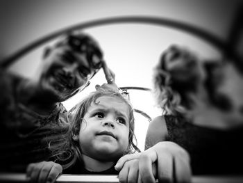 Cute girl looking away while sitting with parents against sky