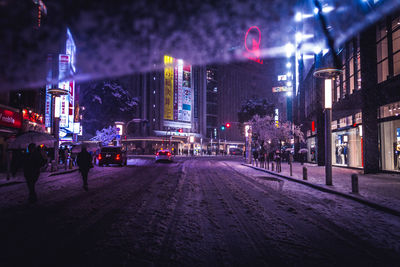 Snow covered street in illuminated city at night