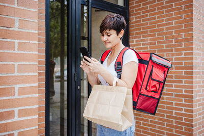 Smiling delivery person using mobile phone while standing by door