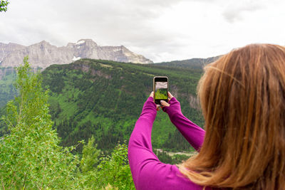 Rear view of woman photographing against mountain
