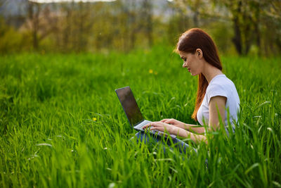 Young woman using laptop while sitting on field