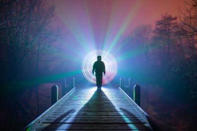 Silhouette man standing against light painting on pier over lake at night