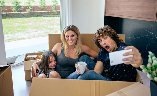 Parents with son taking selfie while sitting in cardboard box at home