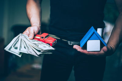 Midsection of man holding paper currency and toy car with model home