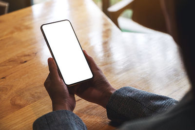 Mockup image of a woman holding mobile phone with blank white desktop screen