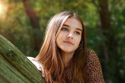 Emotional girl teenager with long hair hairstyle braids in a green shirt sits on a bench in the park