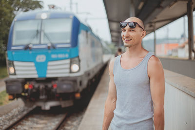 Young man in a t-shirt on the platform waiting for a train using mobile phone. man by train station 