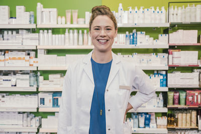 Happy pharmacist with hand on hip standing in chemist shop