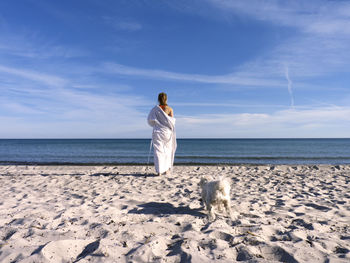 Rear view of woman standing on beach against sky
