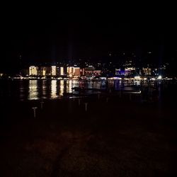 Illuminated buildings by sea against sky at night