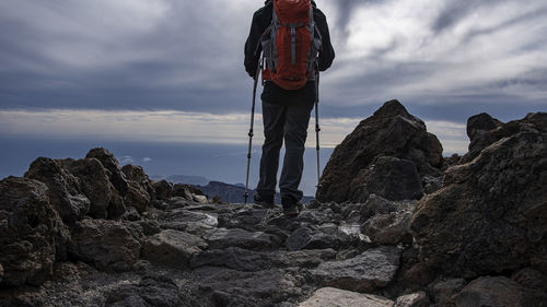 Rear view of man standing on rock against sky