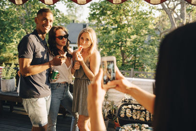 Woman photographing smiling friends on smart phone while enjoying in dinner party