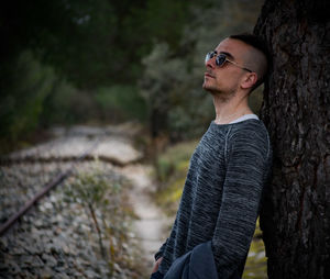 Side view of young man against tree trunk