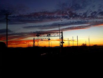 Silhouette electricity pylons on landscape against sky during sunset