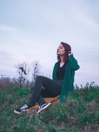 Young woman sitting on field against sky