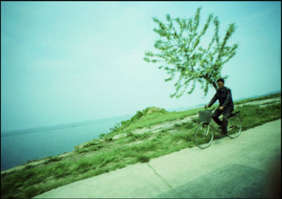 Man riding bicycle by sea against sky