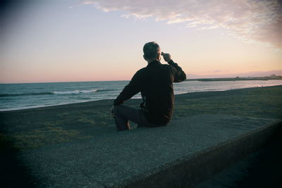 Rear view of man sitting on beach during sunset