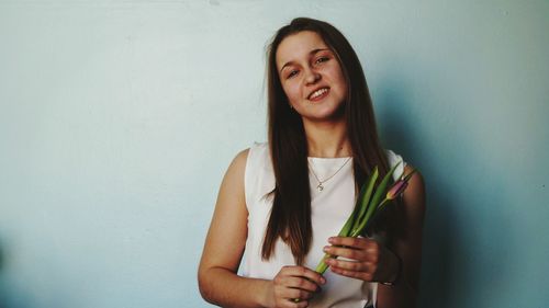 Portrait of smiling woman holding flower against wall