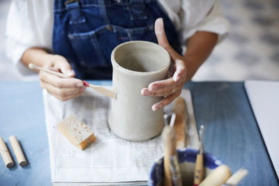 Midsection of mature woman learning pottery at table in art class