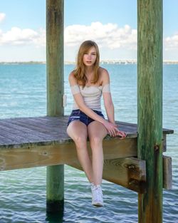 Full length of woman sitting on wooden post against sea