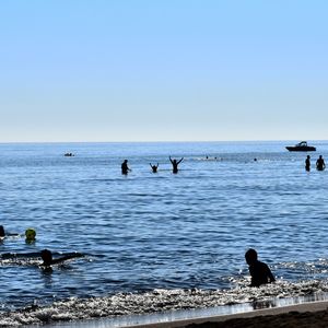 People swimming in sea against clear blue sky