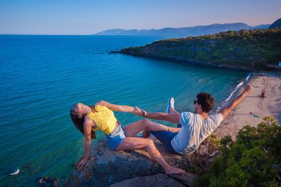 People on rocks by sea against sky