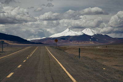 Road leading towards snowcapped mountains against sky