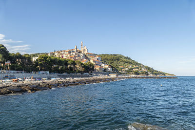 Buildings by sea against blue sky