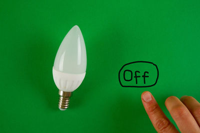 Close-up of hand holding light bulb against green background