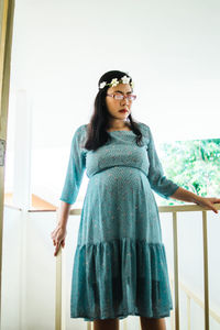 Portrait of young woman standing against window