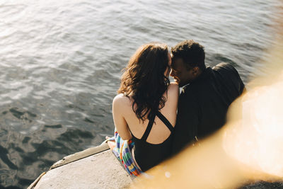 High angle view of affectionate couple sitting on jetty against lake