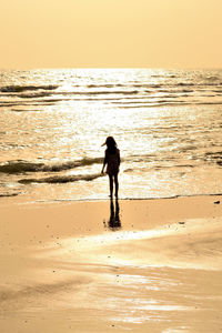 Silhouette woman standing on beach against sky during sunset