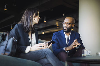 Male and female colleagues discussing while sitting at workplace