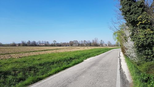 Empty road amidst field against clear blue sky