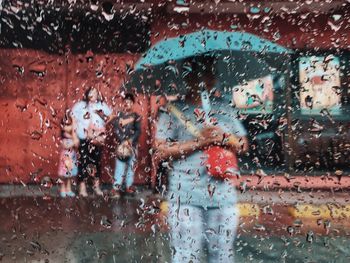 People on street during rain seen through wet glass window