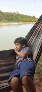 Boy lying on hammock at lakeshore