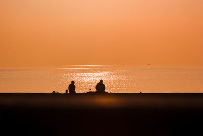 Silhouette people on sea against sky during sunset