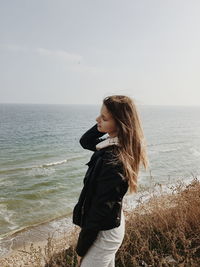 Young woman standing at beach against sky