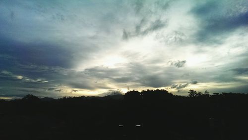 Silhouette trees on landscape against cloudy sky