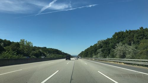 Road by trees against blue sky