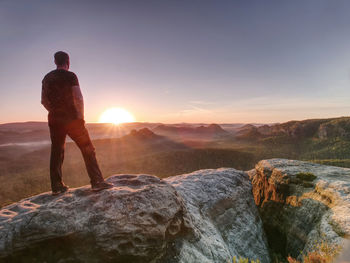 Rear view of man standing on rock against sky during sunset