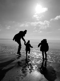 Silhouette family at beach against sky