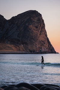 Man surfing on sea against mountain range