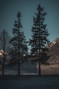 Silhouette trees by lake against sky