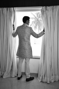 Rear view of couple standing against curtain at home