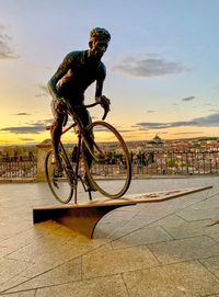 Man riding bicycle on city against sky during sunset