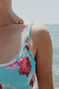 Midsection of woman with seashell on shoulder standing at beach