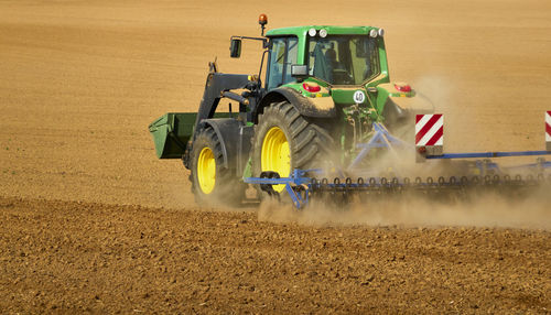 Close-up of a tractor plowing a huge sandy empty field with a cloud of dust