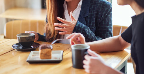 Midsection of woman holding coffee cup on table