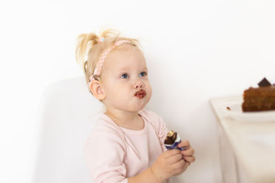 Portrait of cute baby girl eating food against white background